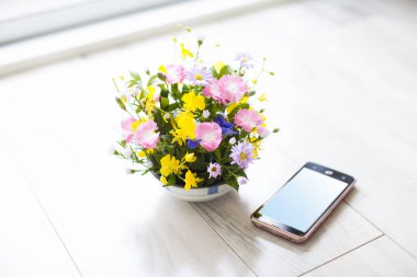 Vazoda güzel çiçekler ve ahşap zeminde akıllı telefon.