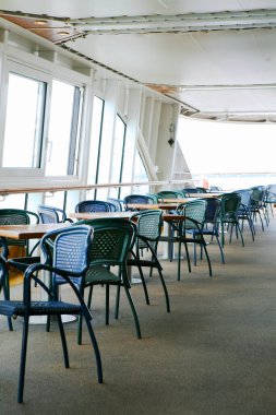Yolcu gemisinin güvertesindeki kafede boş masa ve sandalyeler.    