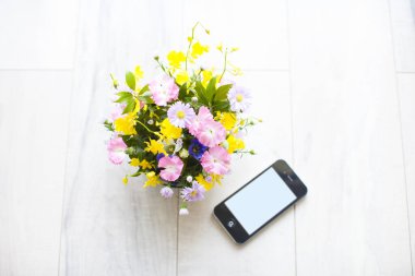 Vazoda güzel çiçekler ve ahşap zeminde akıllı telefon.