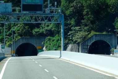 Yol yeşilliklerle çevrili iki karanlık tünele açılıyor.