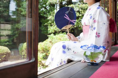 Kağıt yelpaze ve akvaryumlu genç Japon kadın Áwawa 'da oturuyor ve bahçeye bakıyor.