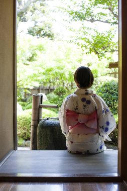 Geleneksel Japon kimonosu giyen genç bir kadın yaz bahçesinde dinleniyor. 