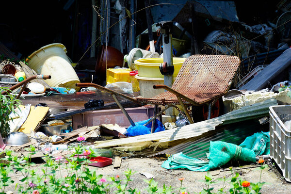 Discarded items cluttering messy outdoor area surrounded by plants