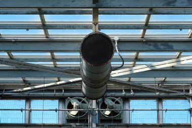 Büyük endüstriyel havalandırma borusu metal sera yapısının içinde asılı.