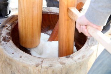 Dışarıdaki ahşap havan içinde yapışkan pirinç dövüyor.