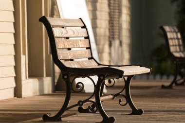 Boş ahşap bank, güneşli veranda boyunca gölgeler bırakıyor.