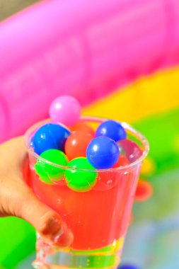 Çocukların elleri renkli küçük toplarla plastik bardakları tutuyor.