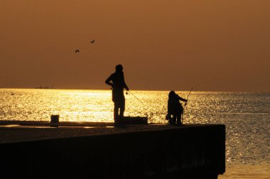 Gün batımında deniz kıyısında balık tutan siluetli insanlar      