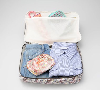 Beyaz arka planda giysi ve aksesuarlarla birlikte açık bavul görüntüsü