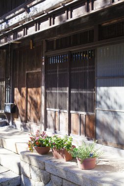 Güneş ışığı kırsal ahşap binaya çarpıyor dış yüzeyde saksı çiçekleri var.