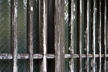 Yıpranmış ahşap parmaklıklar desenli cam pencereleri kaplıyor.