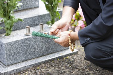 Mezarlıkta mezar taşının yanında dua eden kişi. 