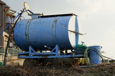 Kırsal binanın yanında duran büyük mavi metal su tankı.