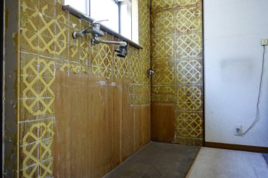 Eski mutfak duvarı açıkta duran boruları gösteriyor sarı fayanslar çıplak ahşap paneller güneş ışığı