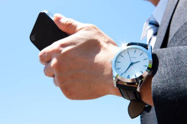Kol saatindeki iş adamının elinde akıllı telefon var.