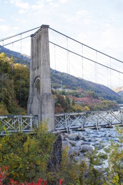 Renkli sonbahar ağaçları arasında kayalık nehri geçen asma köprü