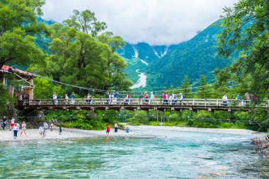 Turistler, Kamikochi, Nagano 'daki Myojin Köprüsü' nde geziyorlar. Etrafı manzaralı dağlarla çevrili..