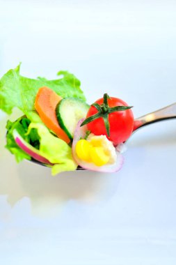 Kaşık içinde taze sebzeli salata, yakın plan. Çeri domates, yumurta, havuç ve salatalık dilimleri, marul yaprakları.