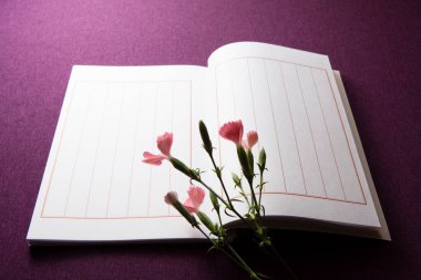 Boş defter sayfaları ve mor arkaplanda pembe karanfil çiçekleri.