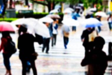 Şehir caddesinde yağmurda yürüyen şemsiyeli insanların bulanık görüntüsü                   
