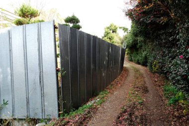Uzun metal çitlerin ve yeşilliklerin yanında dar toprak yol