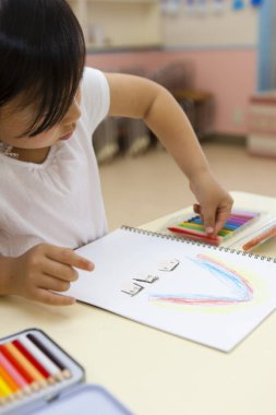 Sınıfta renkli kalemlerle gökkuşağı çizen küçük kız.
