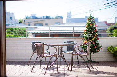 Sandalyeli sehpa ve terasta süslenmiş Noel ağacı.              