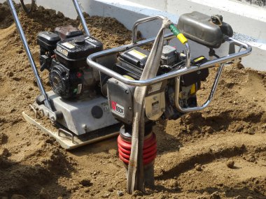 Titreşen plaka sıkıştırıcı ve zıplayan kriko kurcalayıcı dışarıda duruyor.