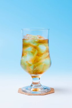 Açık mavi zemin üzerinde buz olan bir bardak soğuk içecek.         