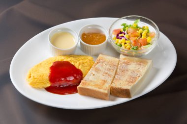 Kahvaltı tabağında omlet, tost salatası ve soslar var.