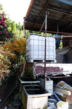 Dışarıdaki yıpranmış konteynırların üzerinde duran büyük plastik su tankı.