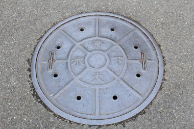 Gri asfalt yüzeyinde dairesel metal rögar kapağı