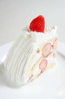 Beyaz tabakta çırpılmış kremayla lezzetli bir çilekli pasta dilimi.