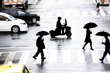 Yağmurlu bir günde şehir caddesinde yürüyen siluetli insanlar        
