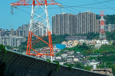 Elektrik iletim kulelerinin arkasında yükselen yüksek apartman binaları yamaçtaki yeşillikler