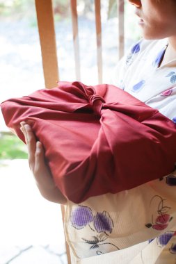 Kırmızı furoshiki sarılı bento tutan kimono giyen genç bir kadın.
