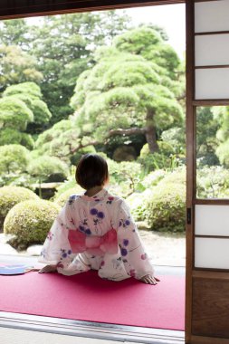 Kimono giyen Japon kadın Anthwa 'da oturuyor ve bahçeye bakıyor.