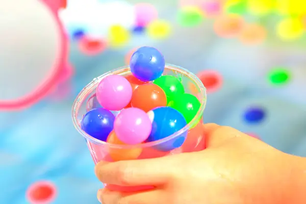 Ręka Dla Dzieci Trzymając Plastikowy Kubek Kolorowe Małe Kulki — Zdjęcie stockowe