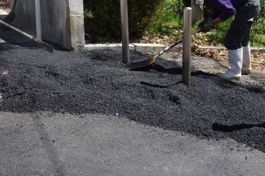 İşçi yol yüzeyine kürek kullanarak asfalt yayıyor.