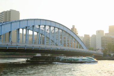 Şehir binaları yakınlarındaki mavi kemer köprüsünün altından tekne geçiyor.