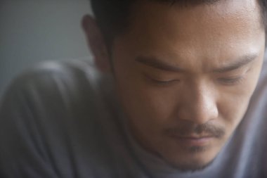 Asyalı üzgün bir adamın aşağı bakan portresi. 