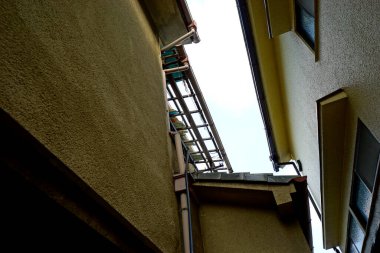 Dar binaların arasından yukarıya metal merdiven gökyüzüne doğru bakıyor.