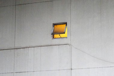 Beton duvardan içeri sıcak sarı ışık saçan küçük açık pencere.