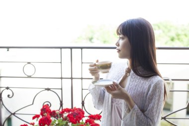 Genç Asyalı kadın balkonda çay içiyor.