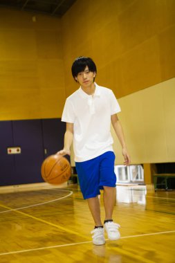 Spor salonunda top eğitimi almış Asyalı basketbolcunun portresi.