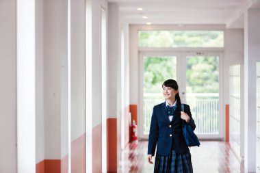 Okul salonunda, üniformalı, çantalı Asyalı bir kızın portresi.