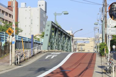 Mavi gökyüzünün altında yeşil metal köprüye doğru kıvrılan sessiz şehir caddesi