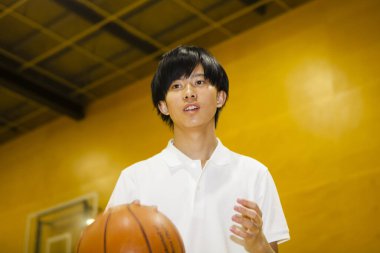 Spor salonunda top eğitimi almış Asyalı basketbolcunun portresi.