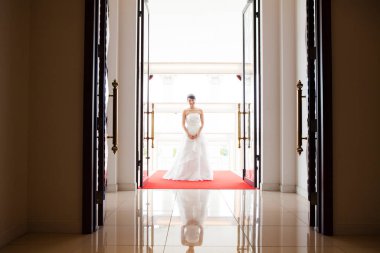 Gelinlik içinde kırmızı halıda duran güzel mutlu gelin.