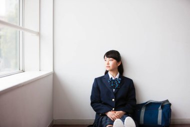 Yerde oturan, üniformalı Asyalı genç bir kızın portresi.